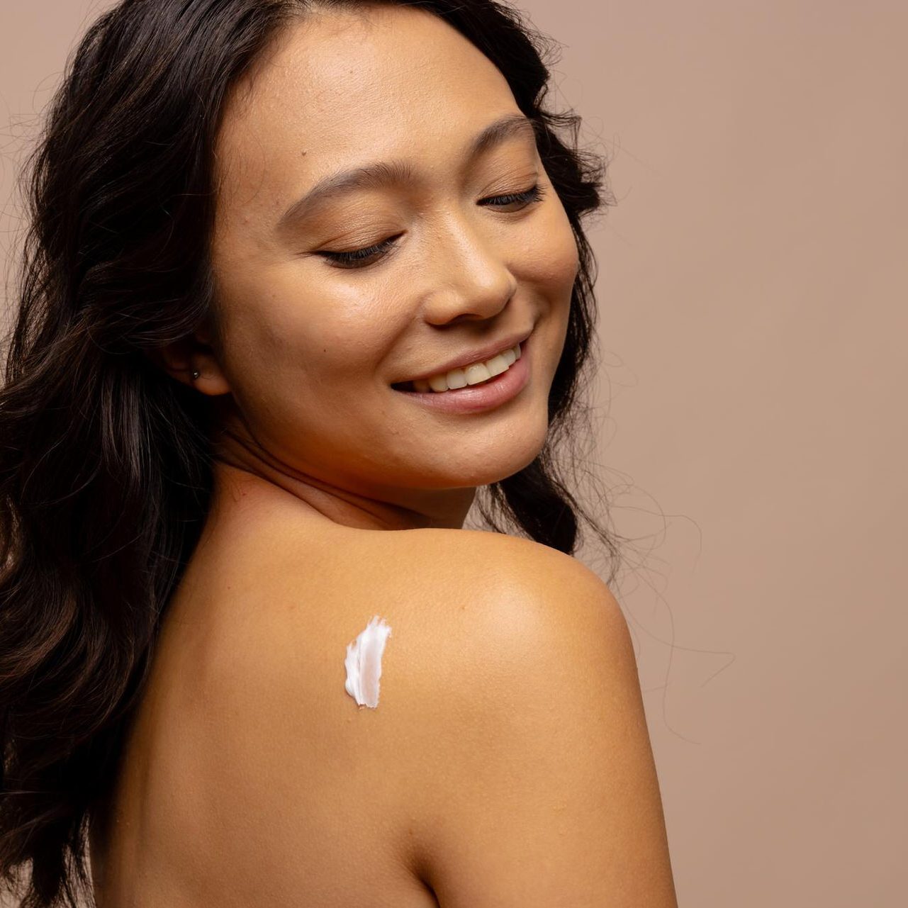 smiling-asian-woman-with-dark-hair-with-skin-cream-her-bare-shoulder-copy-space